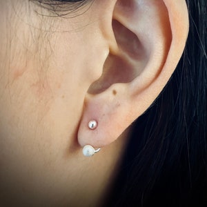May include: A pair of silver earrings with a pearl on one and a small silver ball on the other.