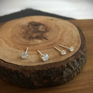 May include: Three silver stud earrings with white opal stones on a wooden surface.