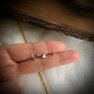 May include: Three gold-toned earrings: a small triangle, a small V-shape, and a small ball.
