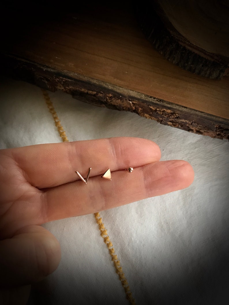 May include: Three gold-toned earrings: a small triangle, a small V-shape, and a small ball.