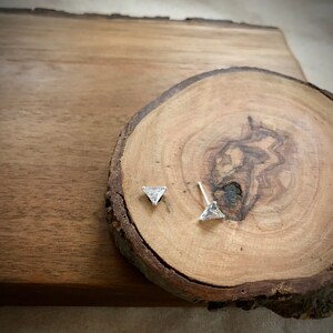 May include: A pair of silver triangle stud earrings with clear cubic zirconia stones on a wooden background.
