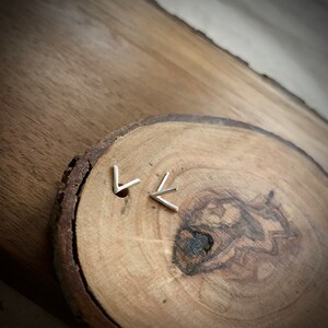 May include: A pair of silver chevron earrings on a wooden surface.