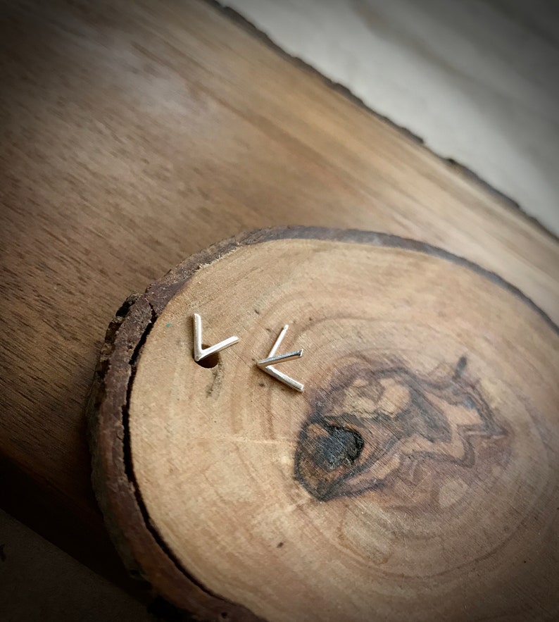 May include: A pair of silver chevron earrings on a wooden surface.