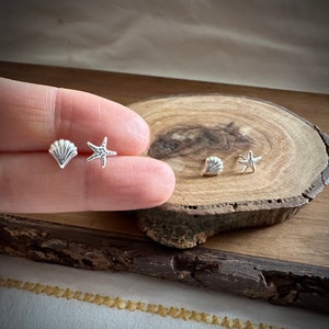 May include: A set of silver earrings featuring a seashell and a starfish design. The earrings are displayed on a wooden surface.