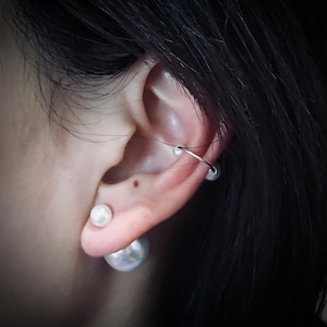 May include: A close-up of a person's ear with two pearl earrings and a silver hoop earring. The earrings are in the shape of a pearl and a hoop.