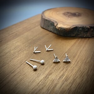 May include: A set of silver earrings with different geometric shapes. The set includes two triangle earrings, two small ball earrings, and two arrow earrings.