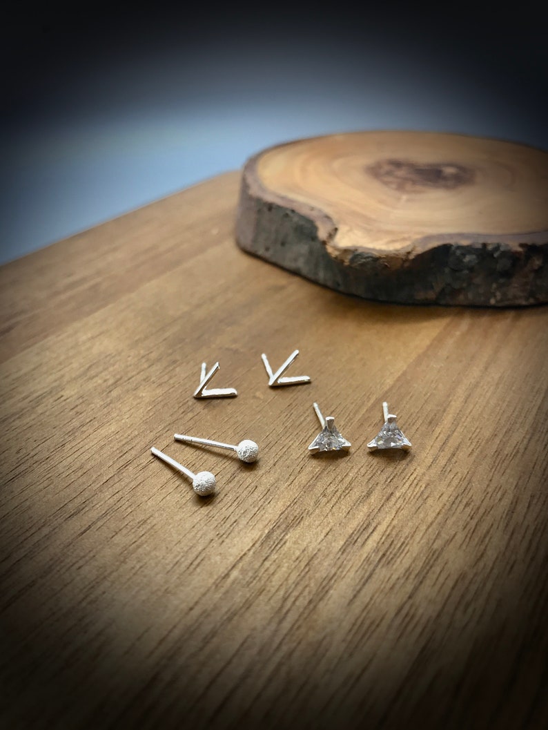 May include: A set of silver earrings with different geometric shapes. The set includes two triangle earrings, two small ball earrings, and two arrow earrings.