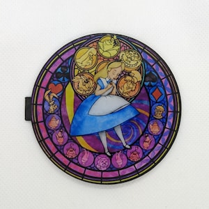 May include: Circular image in a stained-glass style, depicting Alice in Wonderland. Alice, in a blue dress, is the central figure. The design includes characters like the Cheshire Cat and the Mad Hatter, with a black border.