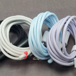 Może przedstawiać: Cztery plecione kable do ładowania w kolorze czarnym, białym, jasnoniebieskim i lawendowym. Kable są zwinięte i mają złącza USB-C.