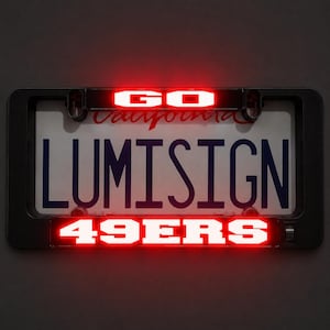 May include: A black rectangular license plate frame featuring integrated LED lighting. The top bar displays the word GO in bright red, while the bottom bar illuminates the text 49ERS in red. The frame surrounds a white California license plate.