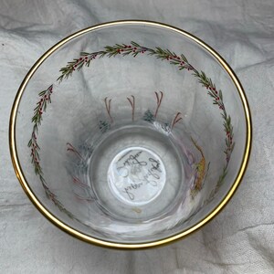 Puede incluir: Vaso de vidrio transparente con borde dorado, con un dise&ntilde;o festivo. El borde est&aacute; acentuado con una banda dorada. El interior tiene un patr&oacute;n decorativo de ramitas verdes con bayas rojas y una escena invernal con esquiadores.