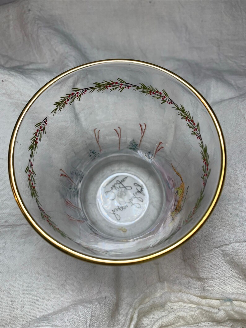 Puede incluir: Vaso de vidrio transparente con borde dorado, con un dise&ntilde;o festivo. El borde est&aacute; acentuado con una banda dorada. El interior tiene un patr&oacute;n decorativo de ramitas verdes con bayas rojas y una escena invernal con esquiadores.