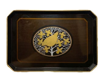 May include: A rectangular black tray with gold trim and a central oval design. The oval features a gold bird perched on a tree with gold and white accents. The tray has a brown background with subtle horizontal lines.