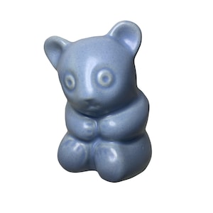 Pode incluir: Estatueta de panda de cerâmica azul clara com acabamento brilhante. O panda está sentado com as patas juntas. Possui olhos grandes e redondos e orelhas pequenas e arredondadas.