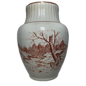 Puede incluir: Jarra de cerámica blanca con una escena de paisaje marrón que representa un árbol, un puente y un bosque. La parte superior de la jarra tiene un diseño acanalado y un borde marrón. Forma bulbosa.