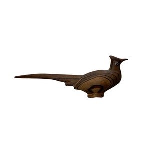 May include: A wooden bird carving in the shape of a pheasant. The bird is brown with dark wood grain and has a long tail.