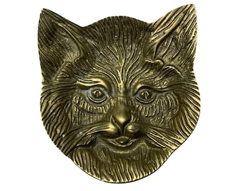 Puede incluir: Un plato de cabeza de gato de latón de color dorado. La cara del gato está detallada con pelo y bigotes.