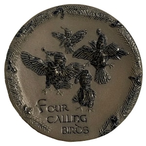 Puede incluir: Un plato redondo de cerámica gris con un diseño en blanco y negro de cuatro pájaros con sombreros. El texto "Four Calling Birds" está escrito en negro en el plato.