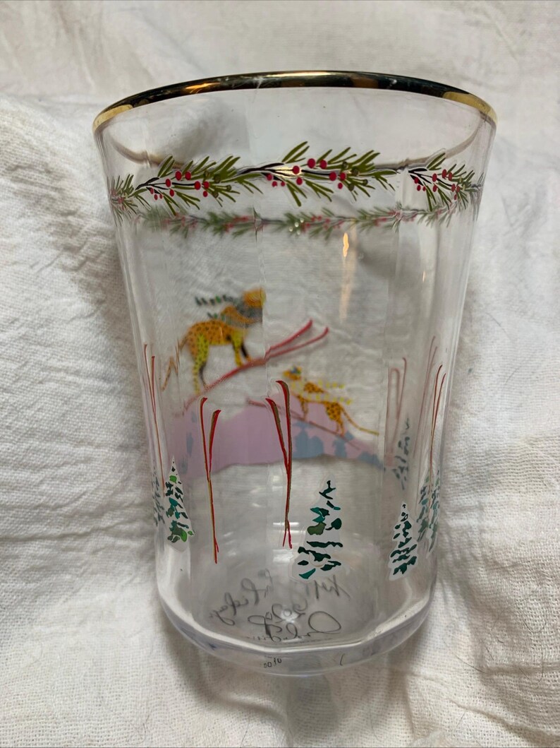 Puede incluir: Vaso de vidrio transparente con borde dorado y dise&ntilde;o de escena invernal. El vaso presenta un esquiador, &aacute;rboles y una guirnalda de hojas verdes y bayas rojas. La parte inferior del vaso tiene texto manuscrito y el a&ntilde;o 2016.