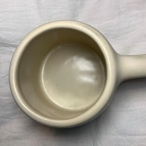 Puede incluir: Taza medidora de cer&aacute;mica color crema con asa. La taza tiene forma de cuenco redondeado y un acabado liso y brillante. El asa est&aacute; fijada al lateral, lo que facilita su sujeci&oacute;n y vertido. Dise&ntilde;ada para medir ingredientes secos o l&iacute;quidos.