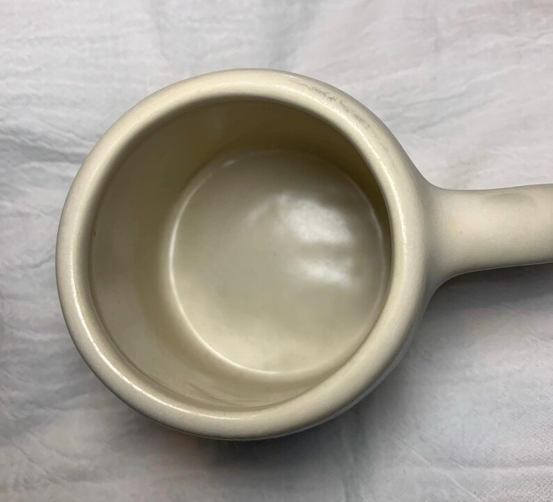 Puede incluir: Taza medidora de cer&aacute;mica color crema con asa. La taza tiene forma de cuenco redondeado y un acabado liso y brillante. El asa est&aacute; fijada al lateral, lo que facilita su sujeci&oacute;n y vertido. Dise&ntilde;ada para medir ingredientes secos o l&iacute;quidos.