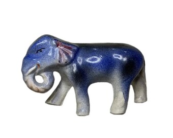 Può includere: Una statuetta di elefante in ceramica blu e bianca con la proboscide arrotolata. L'elefante ha una smaltatura blu macchiata e accenti rosa sulle orecchie.
