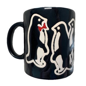May include: Black ceramic mug featuring a repeating penguin design. The penguins are black with white outlines and accents, and some have a red bow tie. The mug has a black handle and a glossy finish.