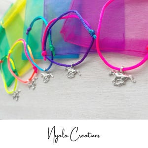 May include: A selection of vibrant cord bracelets, each featuring a silver horse charm. The bracelets come in pink, purple, blue, green, and yellow. They are presented on a white surface, with colourful sheer bags in the background. The text "Nyala Creations" is visible at the bottom.