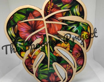 May include: A wooden cutout of a monstera leaf with a tropical floral print. The print features red, orange, yellow, and green flowers and leaves.