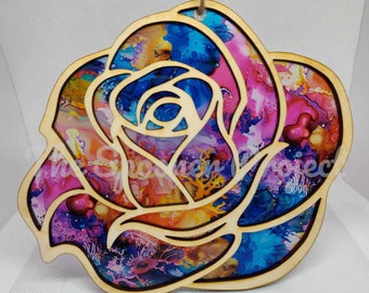 May include: A wooden rose ornament with a colorful abstract design. The rose is cut out and the background is a light wood color.