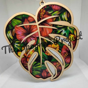 May include: A wooden cutout of a monstera leaf with a tropical floral print. The print features red, orange, yellow, and green flowers and leaves.