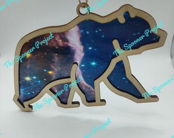 May include: Wooden bear ornament with a galaxy design. The bear is cut out and the galaxy design is visible through the cutout. The ornament has a string for hanging.