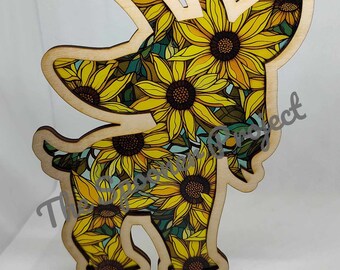 May include: Wooden cutout of a goat with a sunflower pattern. The goat is standing on all four legs and has a long, curved horn. The sunflower pattern is yellow and green.