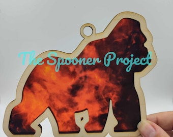 May include: Wooden ornament shaped like a gorilla with a red, orange, and black tie-dye pattern. The ornament has a hole at the top for hanging.