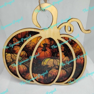 May include: Wooden pumpkin ornament with a stained glass design featuring a variety of orange, yellow, and brown pumpkins. The ornament has a loop at the top for hanging.