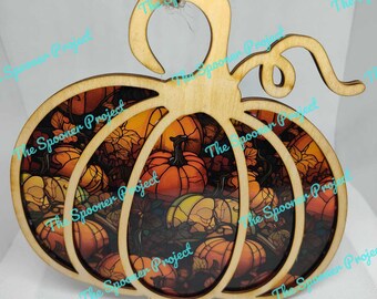 May include: Wooden pumpkin ornament with a stained glass design featuring a variety of orange, yellow, and brown pumpkins. The ornament has a loop at the top for hanging.