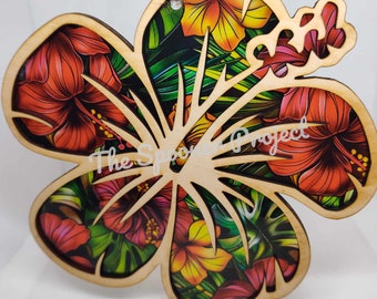 May include: A wooden cutout of a hibiscus flower with a tropical print inside. The flower is painted in shades of red, yellow, and green. The text "The Spoon Project" is visible in the center of the flower.