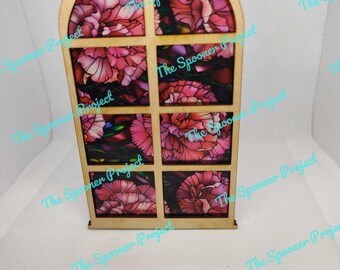 May include: A wooden window-shaped ornament with a stained glass design featuring pink flowers. The ornament has a loop at the top for hanging.