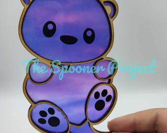 May include: A purple and pink ombre wooden cutout of a cartoon otter with black paw prints. The otter is holding its tail in its paws and has a cute expression on its face.