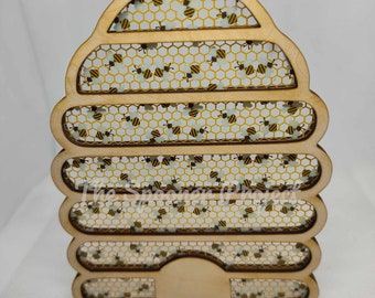 May include: Wooden beehive ornament with a honeycomb pattern and small bees. The ornament is light brown and has a string for hanging.