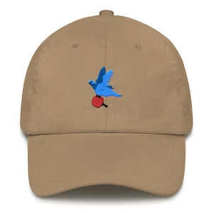 May include: A tan baseball cap with an embroidered blue bird holding a red ping pong paddle.