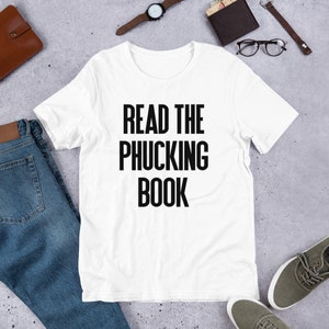 May include: White t-shirt with black text that reads "READ THE PHUCKING BOOK".