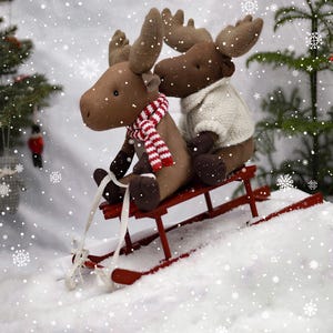 May include: Two brown plush moose toys riding on a red wooden sled in a snowy winter scene.