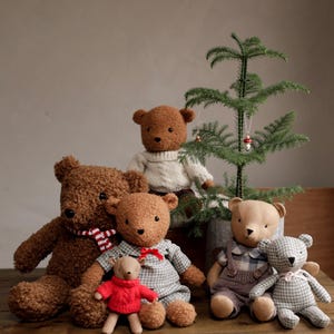 May include: A group of six plush teddy bears in various poses. The bears are brown, beige, and gray with different patterns and textures. The bears are sitting in front of a small potted Christmas tree with red ornaments.
