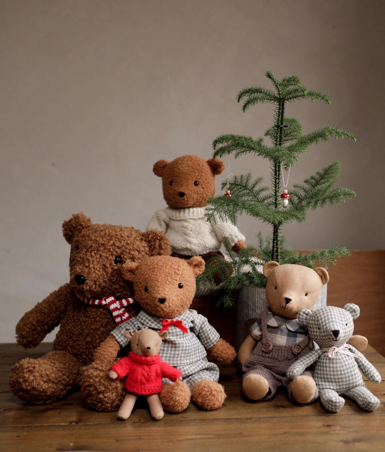 May include: A group of six plush teddy bears in various poses. The bears are brown, beige, and gray with different patterns and textures. The bears are sitting in front of a small potted Christmas tree with red ornaments.