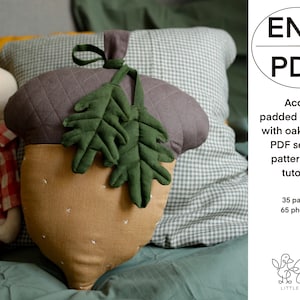 Könnte beinhalten: Ein braunes und grünes Kissen in Form einer Eichel mit Eichenblättern. Das Kissen ist aus Stoff und hat eine gesteppte Textur. Das Bild enthält den Text "ENG PDF Acorn padded cushion with oak leaves PDF sewing pattern and tutorial 35 pages 65 photos LITTLE THINGS".