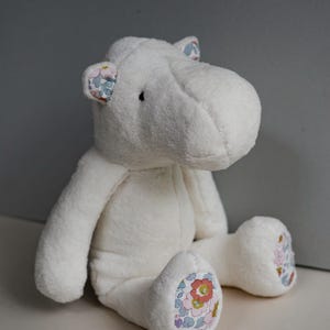 May include: White plush hippopotamus stuffed animal with floral fabric accents on the ears and feet.