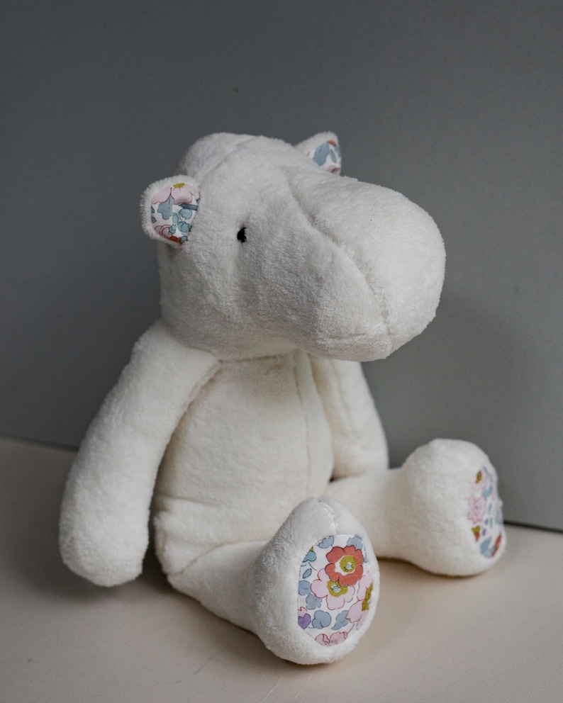 May include: White plush hippopotamus stuffed animal with floral fabric accents on the ears and feet.