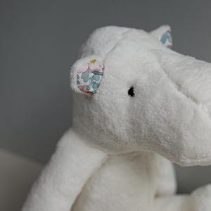 May include: White plush hippopotamus toy with floral fabric ears. The toy has a soft, cuddly texture and is perfect for children.