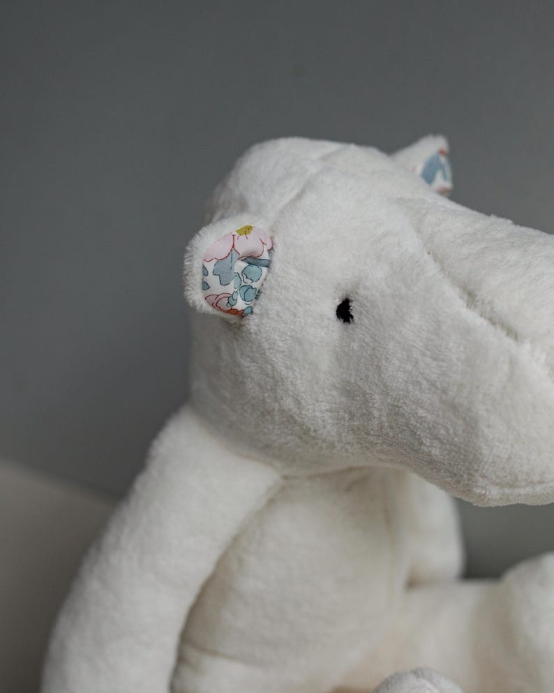 May include: White plush hippopotamus toy with floral fabric ears. The toy has a soft, cuddly texture and is perfect for children.